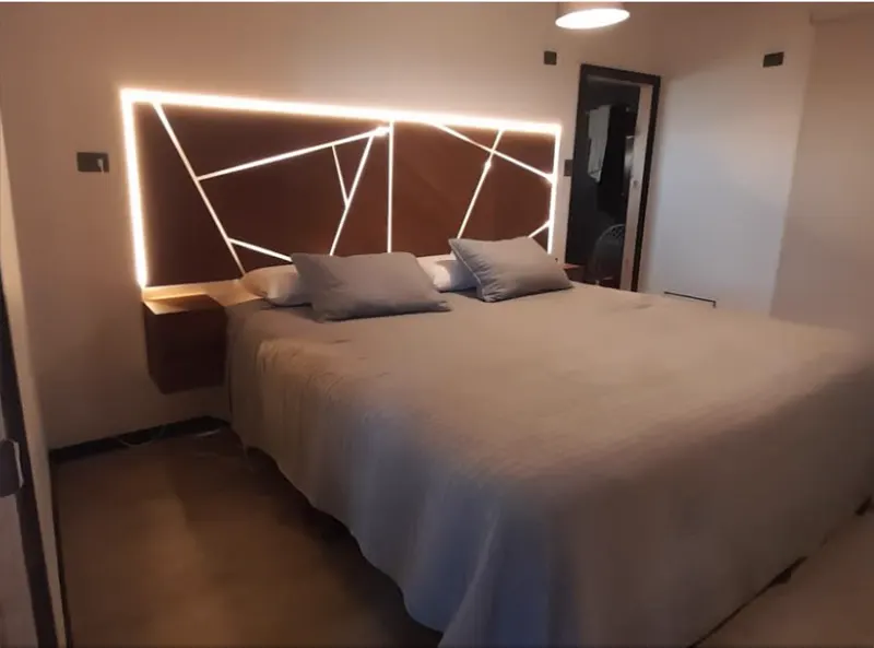 Respaldo de cama a medida en tablero Nogal Amazónico con líneas geométricas retroiluminadas y veladores flotantes integrados