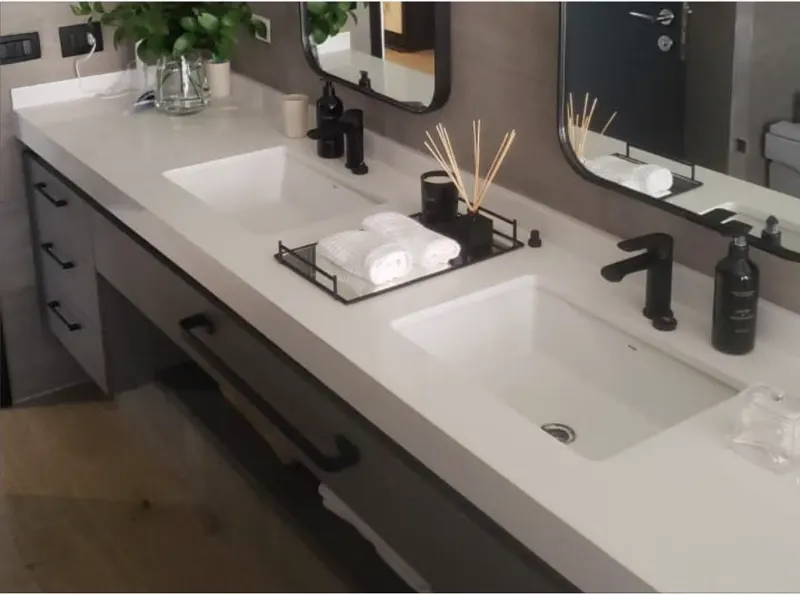 Vanitorio flotante de baño en tablero Fibra con cubierta blanca continua, dos fuentones de losa bajo cubierta y grifería negra